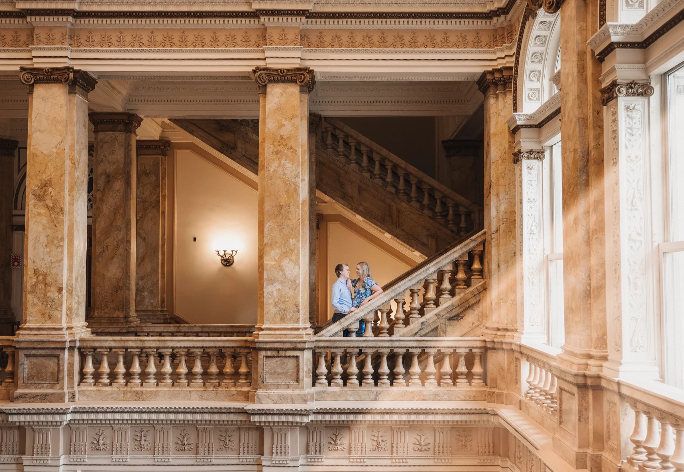 Gabriella and Jameson sitting together inside an ornate sunlit hall.